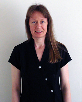 Heather Costello, smiling, in a black tunic against a plain white wall